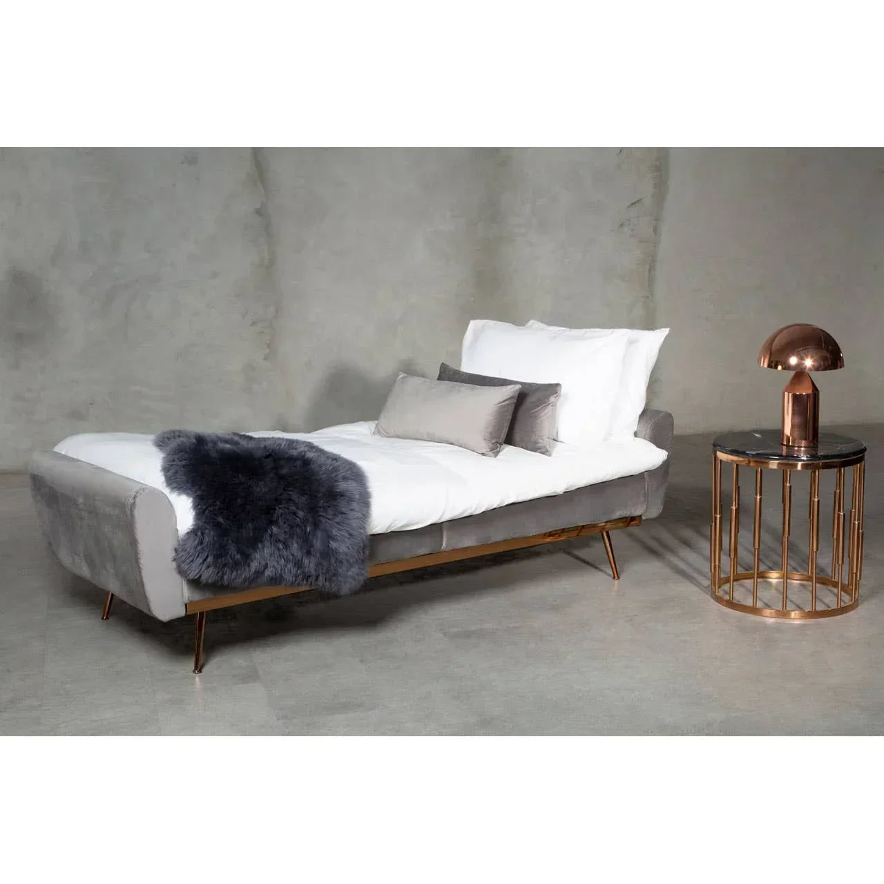 Grey velvet daybed with gold legs, white bedding and cushions, next to a round side table