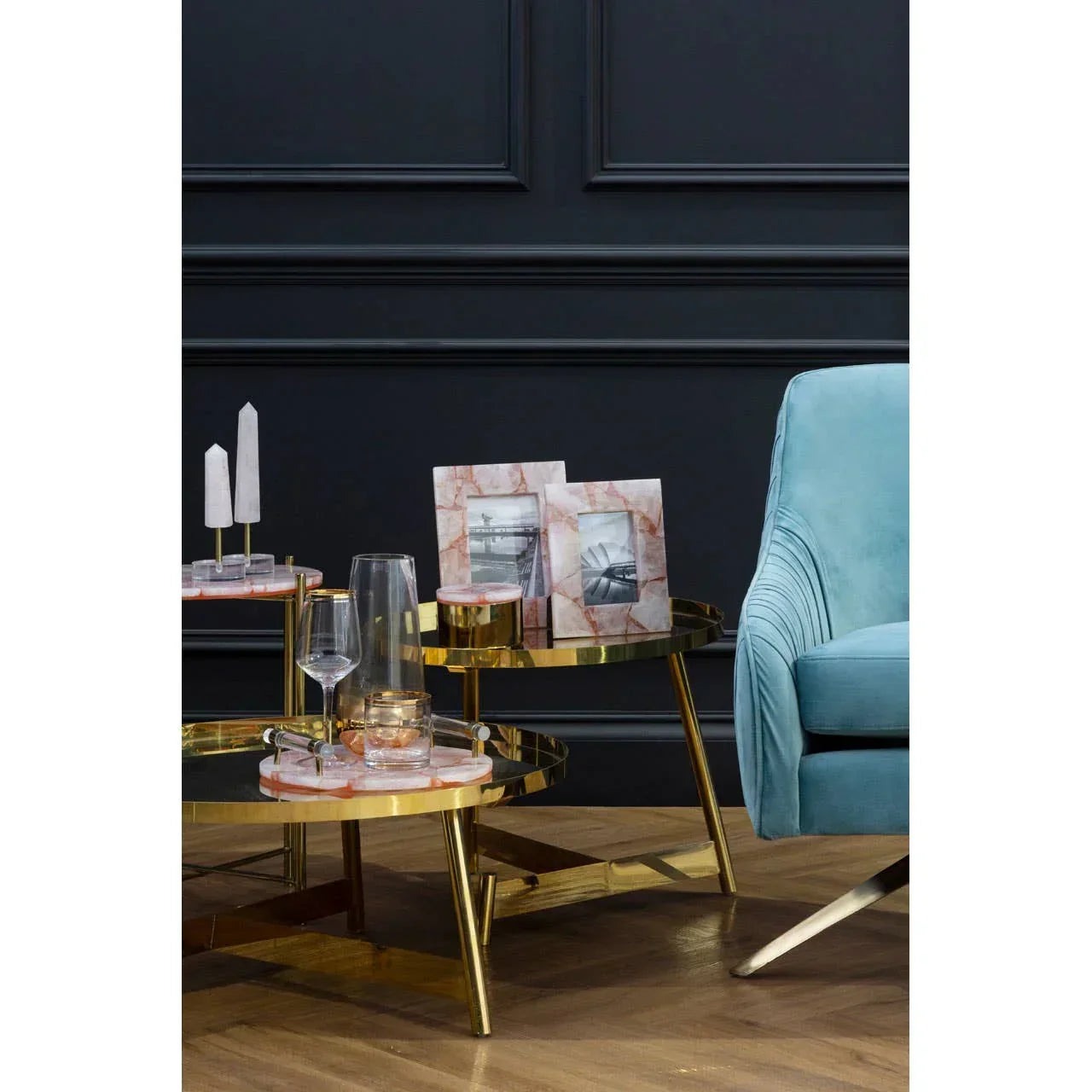 Gold and marble nesting coffee tables with decor beside blue velvet armchair on wood floor
