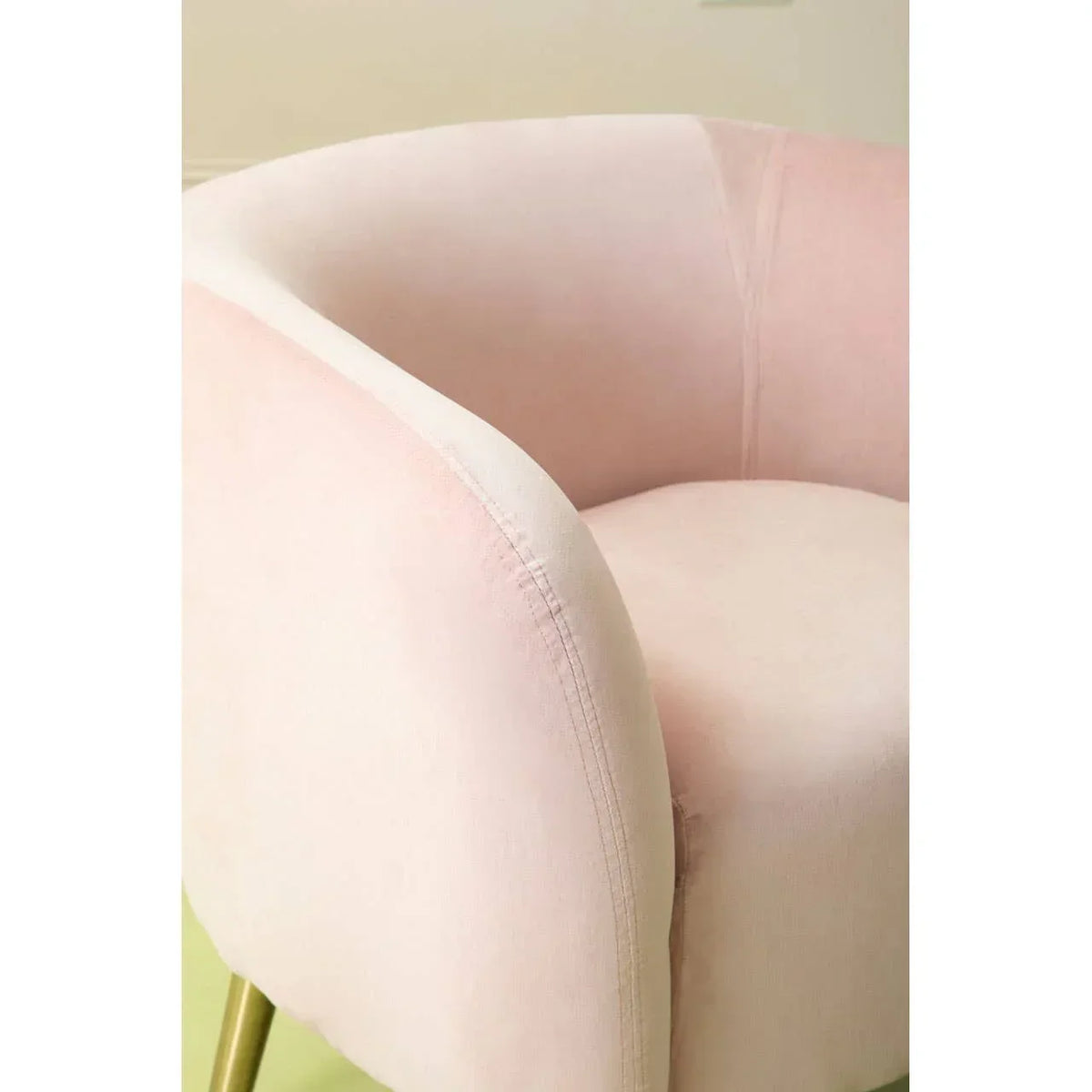 Blush pink velvet accent chair with curved backrest and gold legs, close-up view
