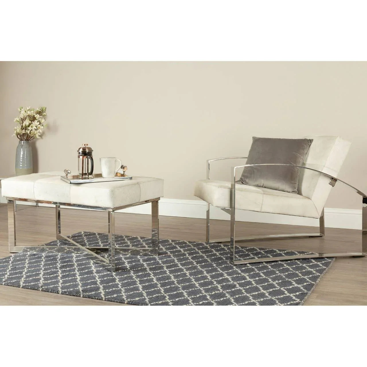 Modern armchair with chrome frame and cream upholstery beside matching footstool on patterned rug