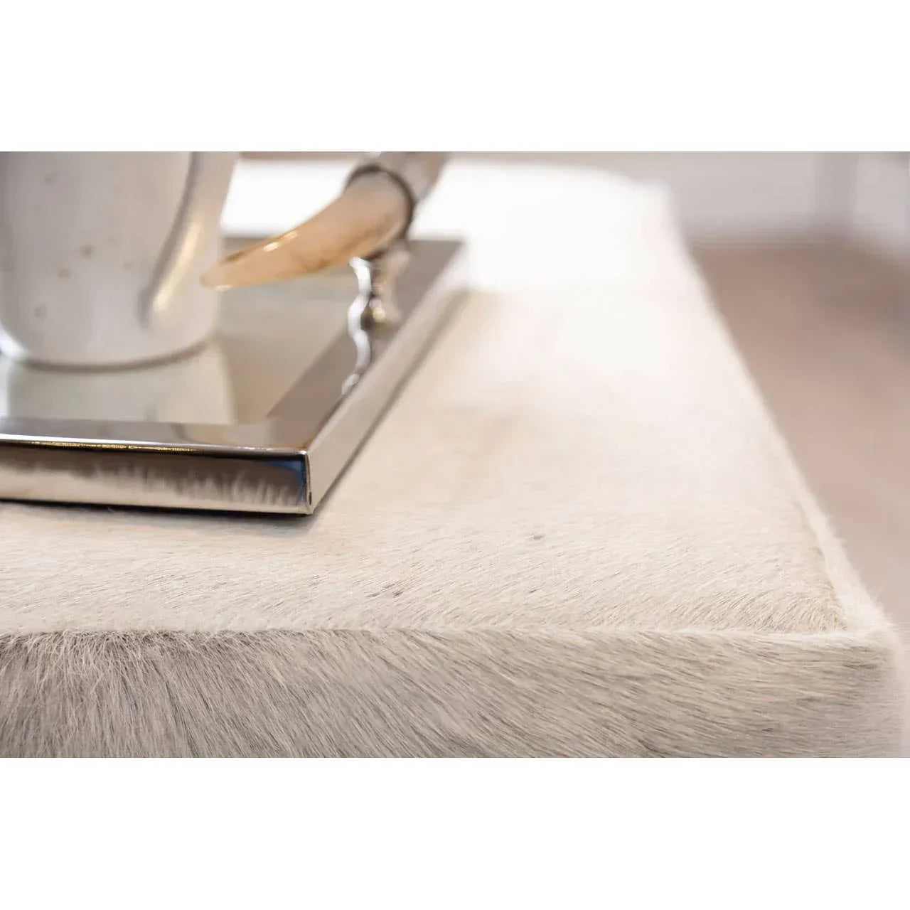Close-up of white cowhide ottoman with silver tray and coffee cup on top