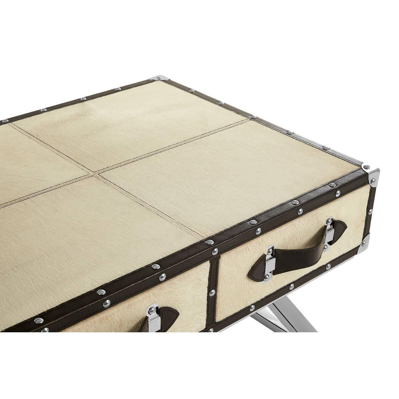 Beige faux leather trunk coffee table with metal rivet details and dark handles, corner view