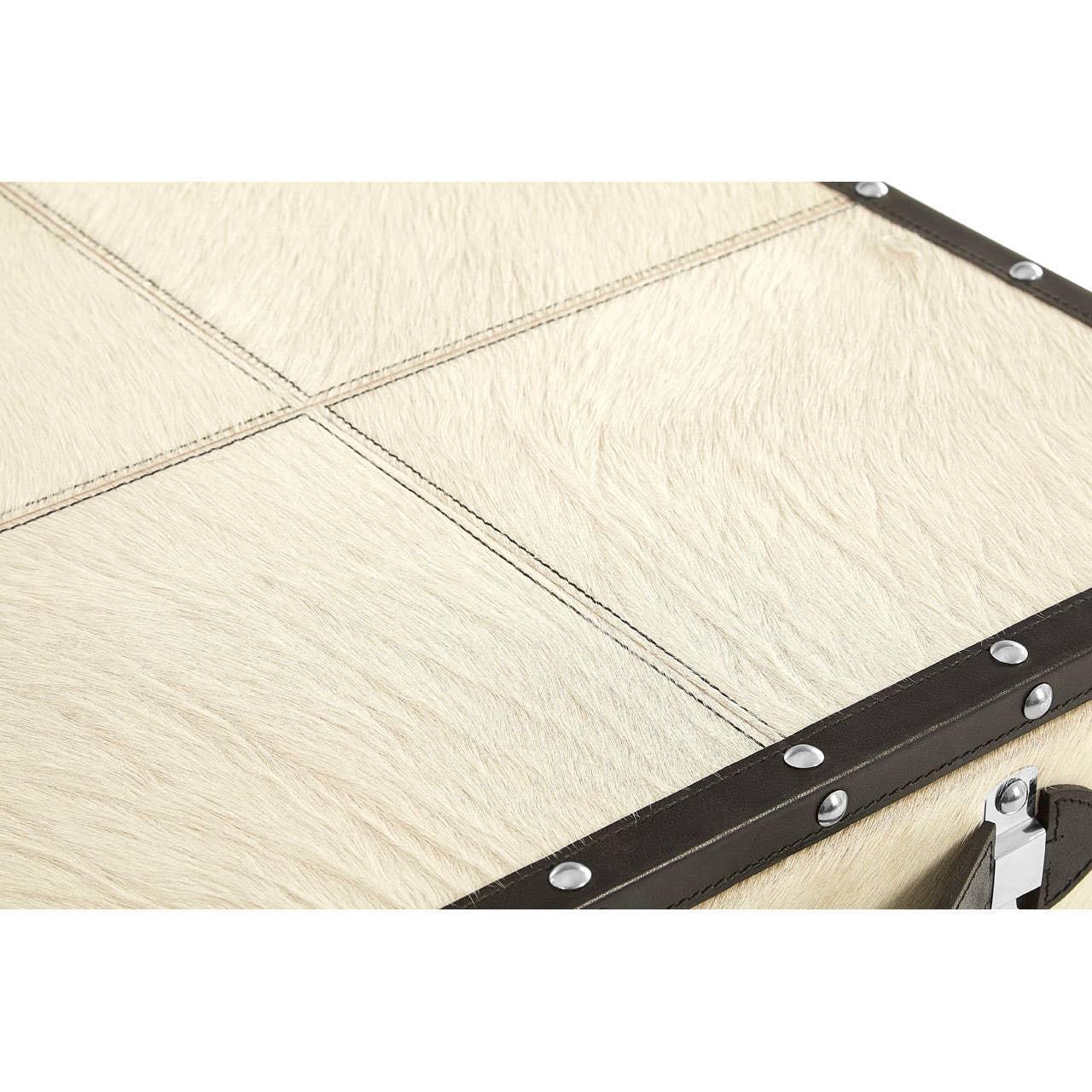 Close up of cream cowhide storage trunk lid with dark leather trim and metal studs