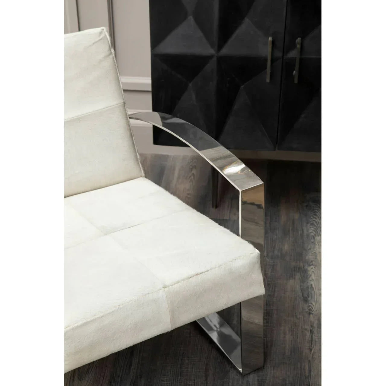 Modern armchair with chrome armrest and white upholstered seat on wooden floor