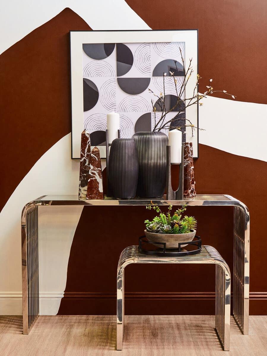 Chrome console table with matching stool, vases, candles and succulents against brown wall