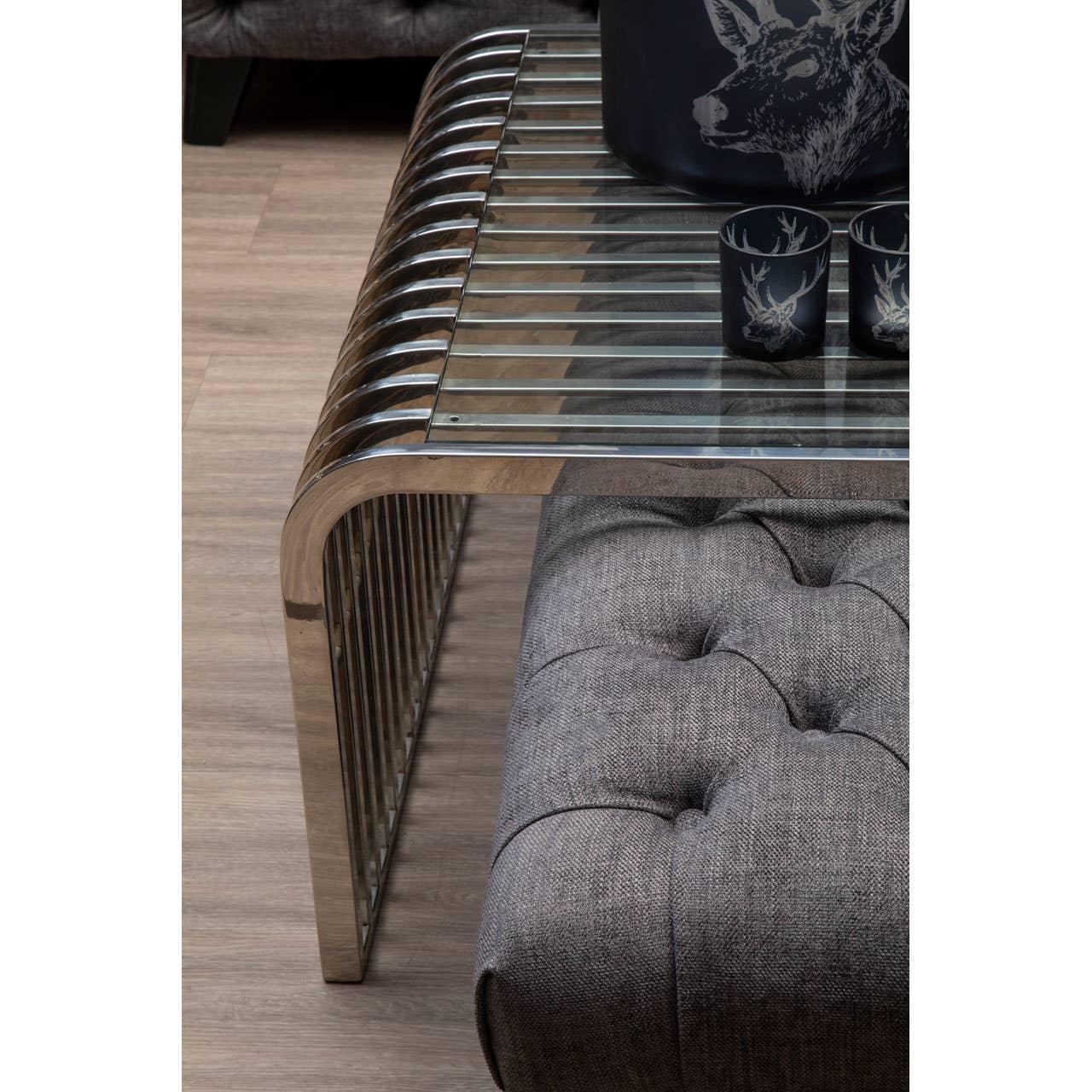 Glass and chrome coffee table with tufted grey ottoman on wood floor
