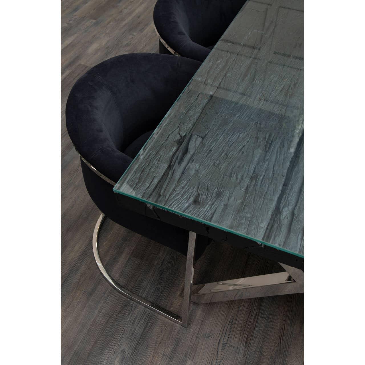 Glass dining table with textured stone surface and black velvet chairs on wooden floor