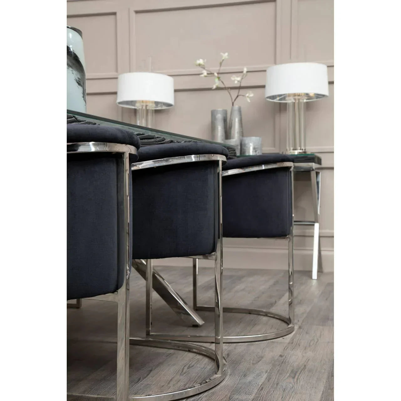 Black velvet dining chairs with chrome legs beside glass table on wooden floor