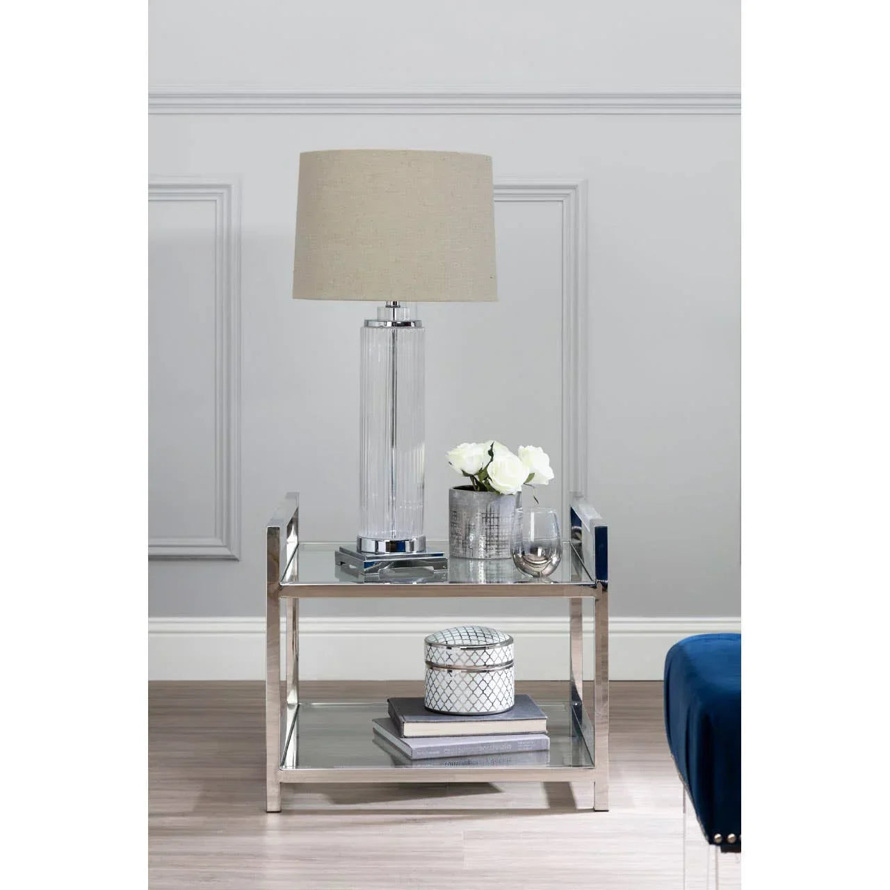 Glass and chrome side table with table lamp, white flowers, and decorative jars
