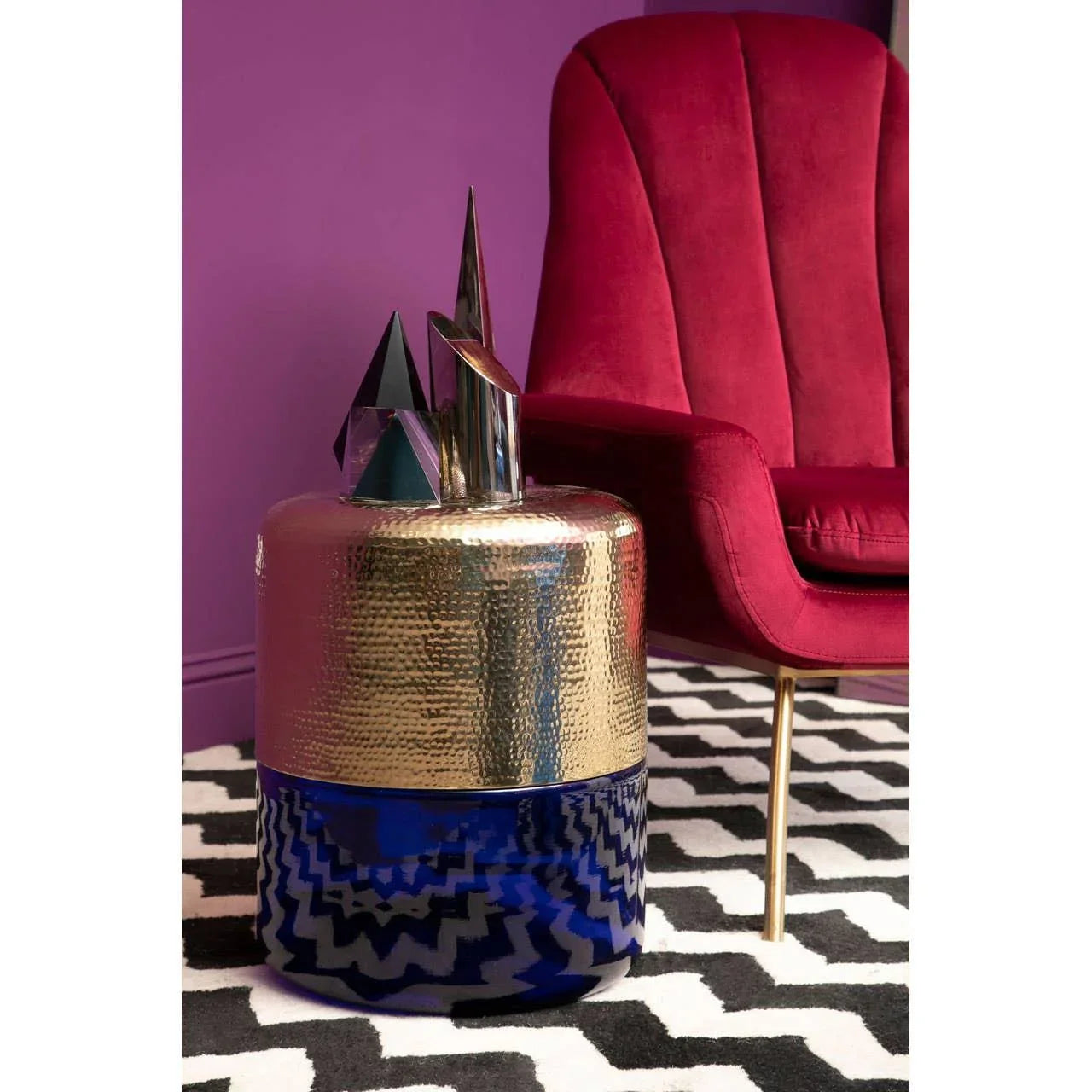 Gold and blue side table beside red velvet accent chair on patterned rug