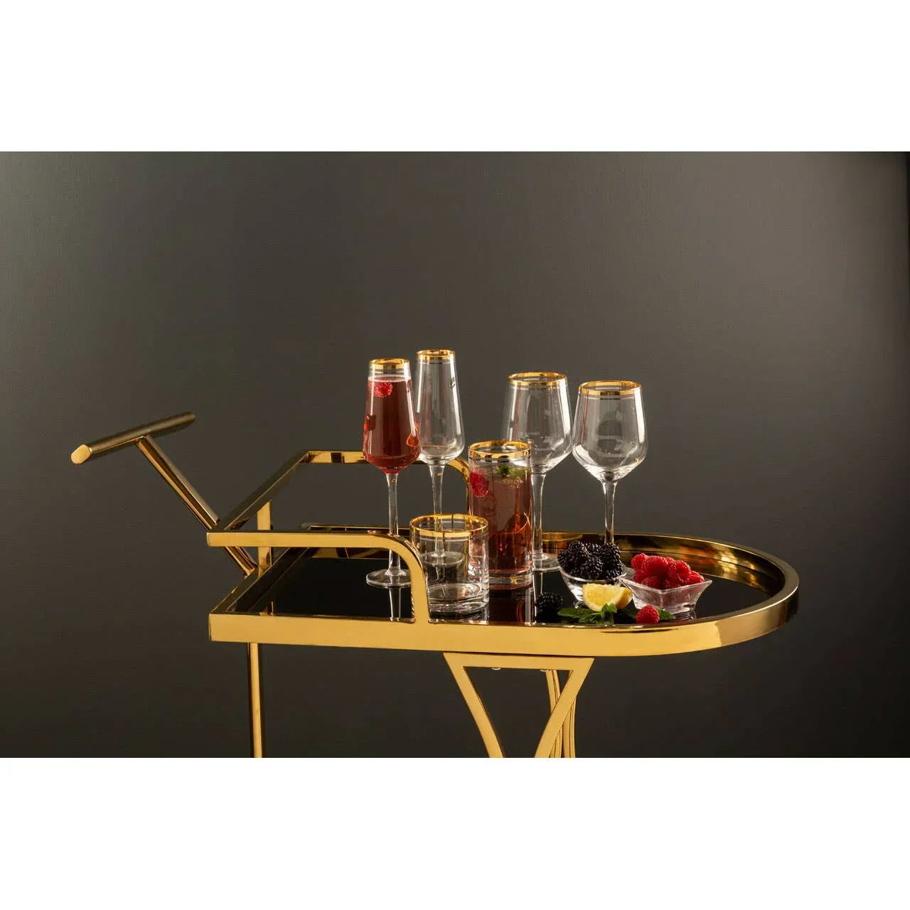 Gold serving trolley with glassware, drinks, and fruit on black mirrored tray