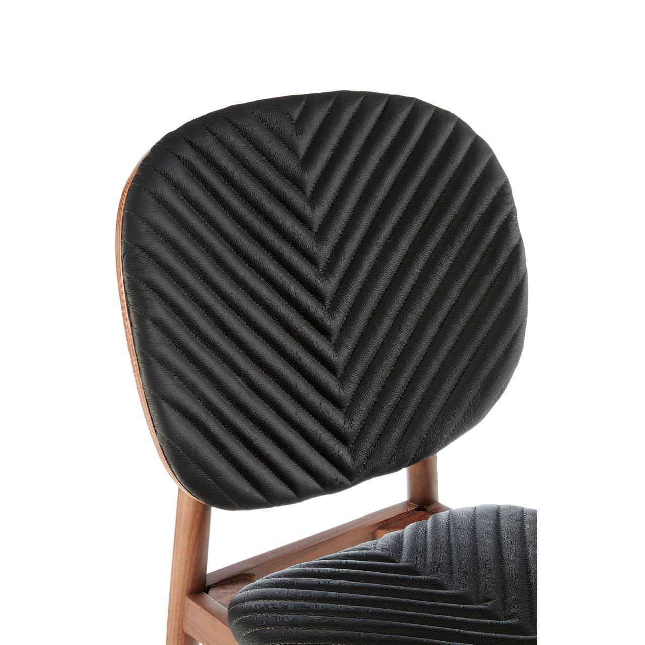 Black chevron-stitched dining chair backrest with wooden frame close up