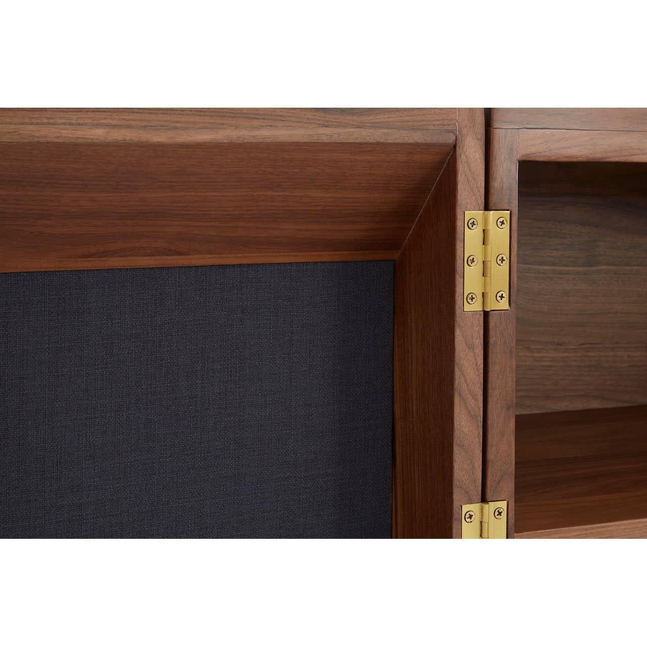 Close detail walnut cabinet door with brass hinges and black textured panel