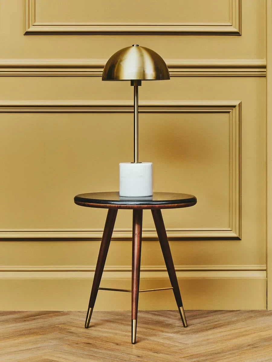 Round wooden side table with gold floor lamp and marble base against yellow panel wall