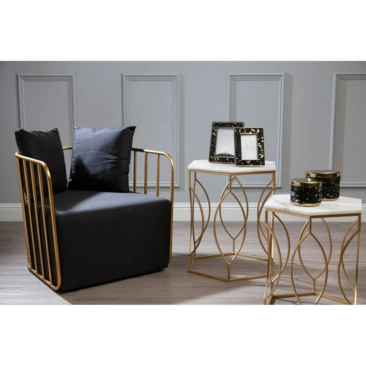 Gold metal armchair with black cushions beside two marble top side tables in living room