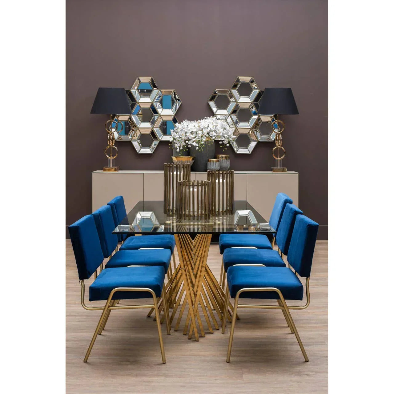 Glass dining table with gold legs and six blue velvet chairs in modern dining room