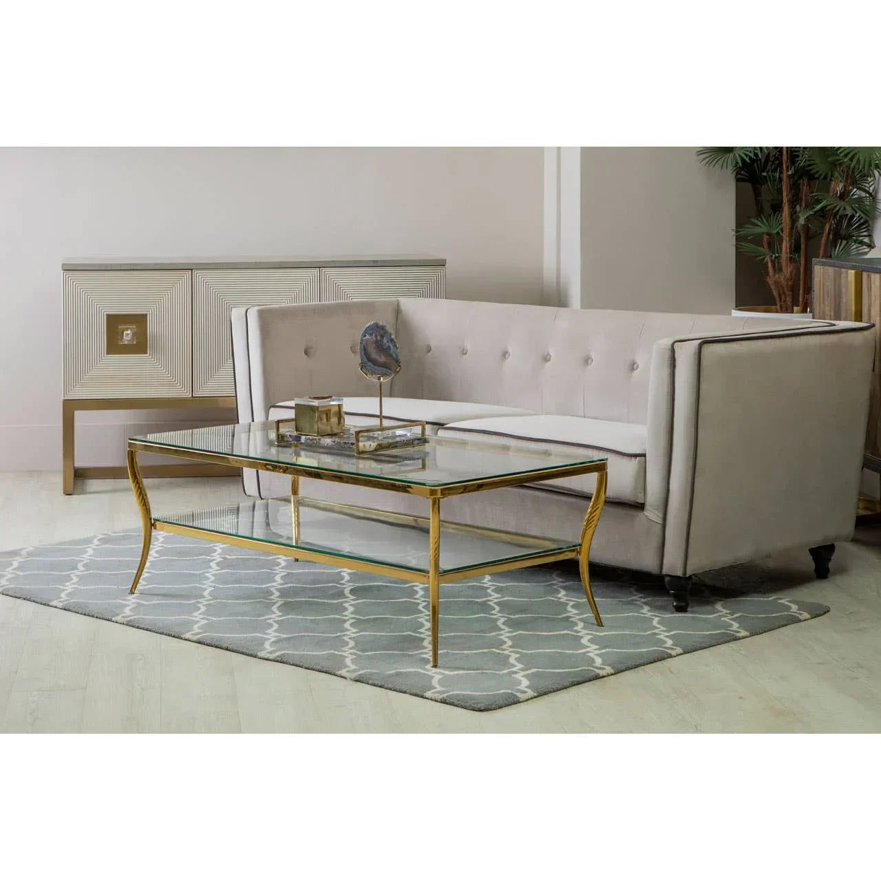 Beige velvet sofa with button tufting, gold glass coffee table on patterned rug in living room