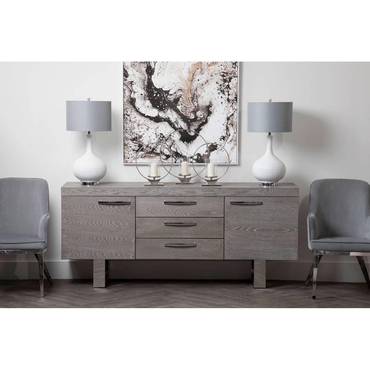 Grey sideboard with drawers and cabinets, flanked by chairs, topped with lamps and decor