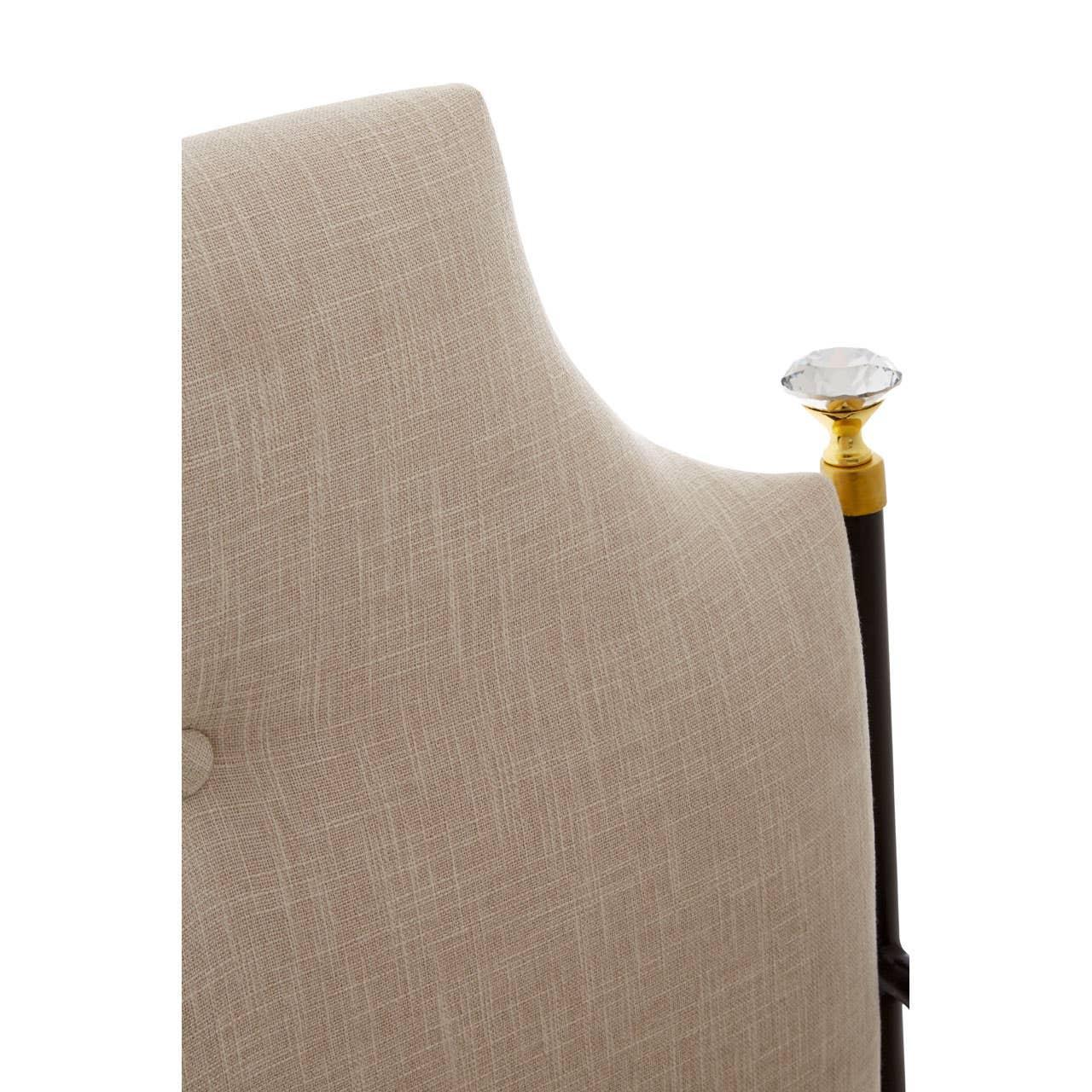 Beige upholstered dining chair with button detail and gold finial accent on backrest