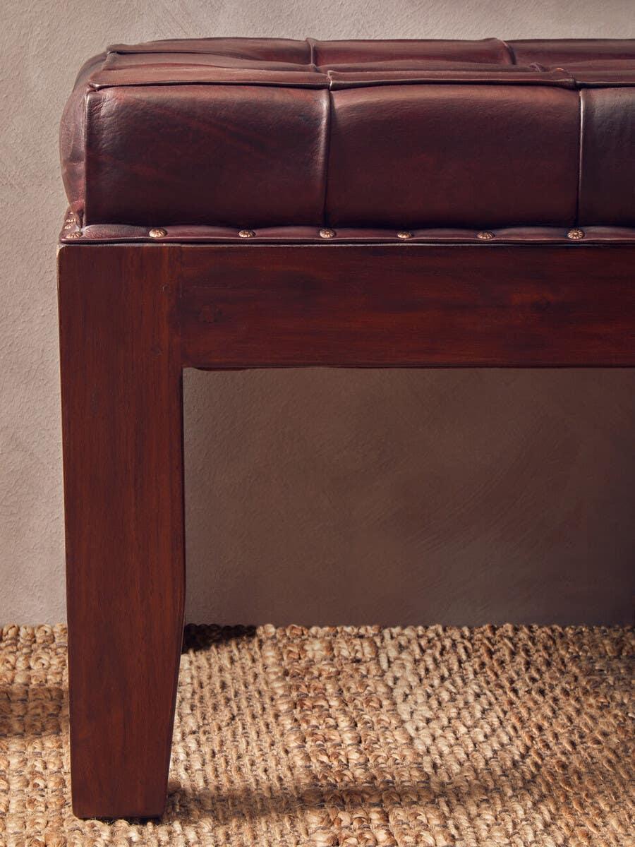 Brown leather bench with wooden legs on woven rug, close-up of corner detail