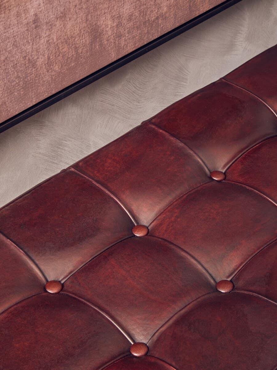 Close-up of dark brown leather sofa seat with tufted button details and textured wall behind
