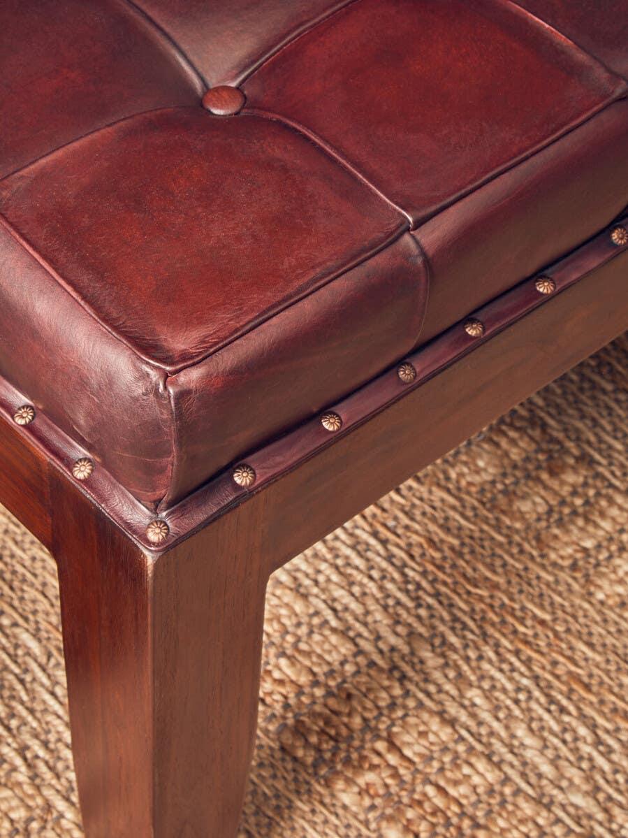 Brown leather ottoman with tufted top and wooden legs on a woven rug