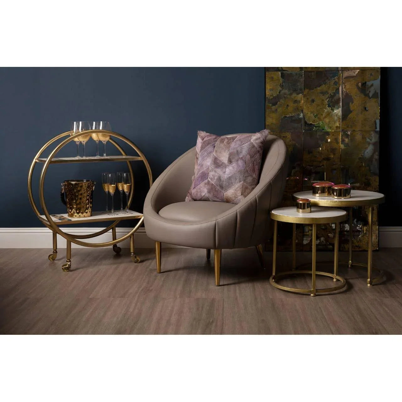 Contemporary grey accent chair with gold legs beside round marble and gold side tables