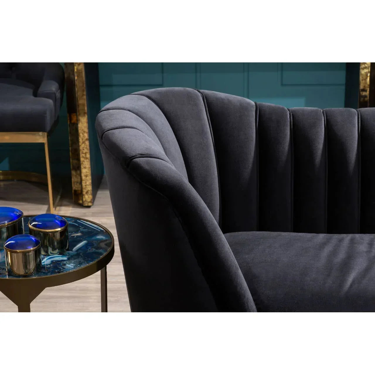Dark grey velvet sofa with scalloped backrest next to round side table with blue accents