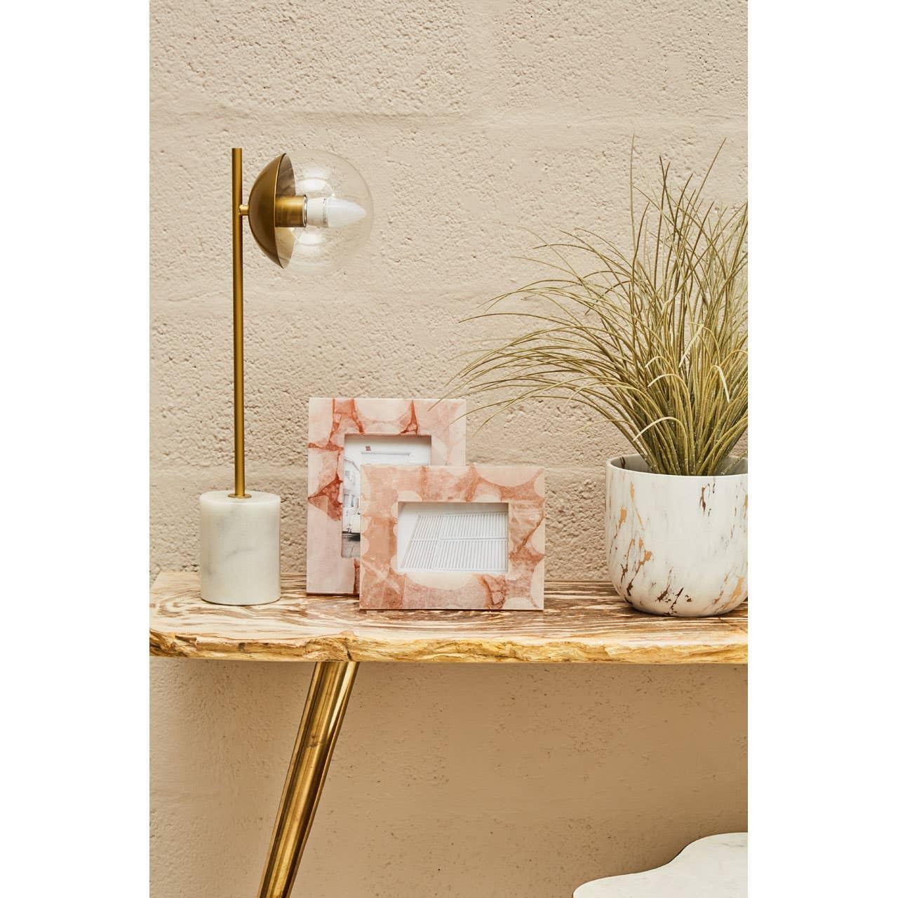 Pink marble photo frames with decorative lamp and plant on wooden console table
