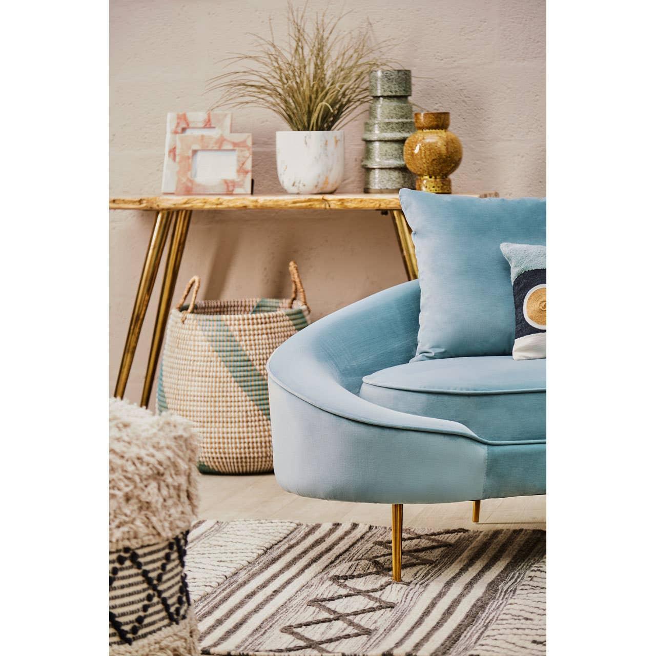 Blue velvet sofa with gold legs beside woven basket and decorative side table in living room