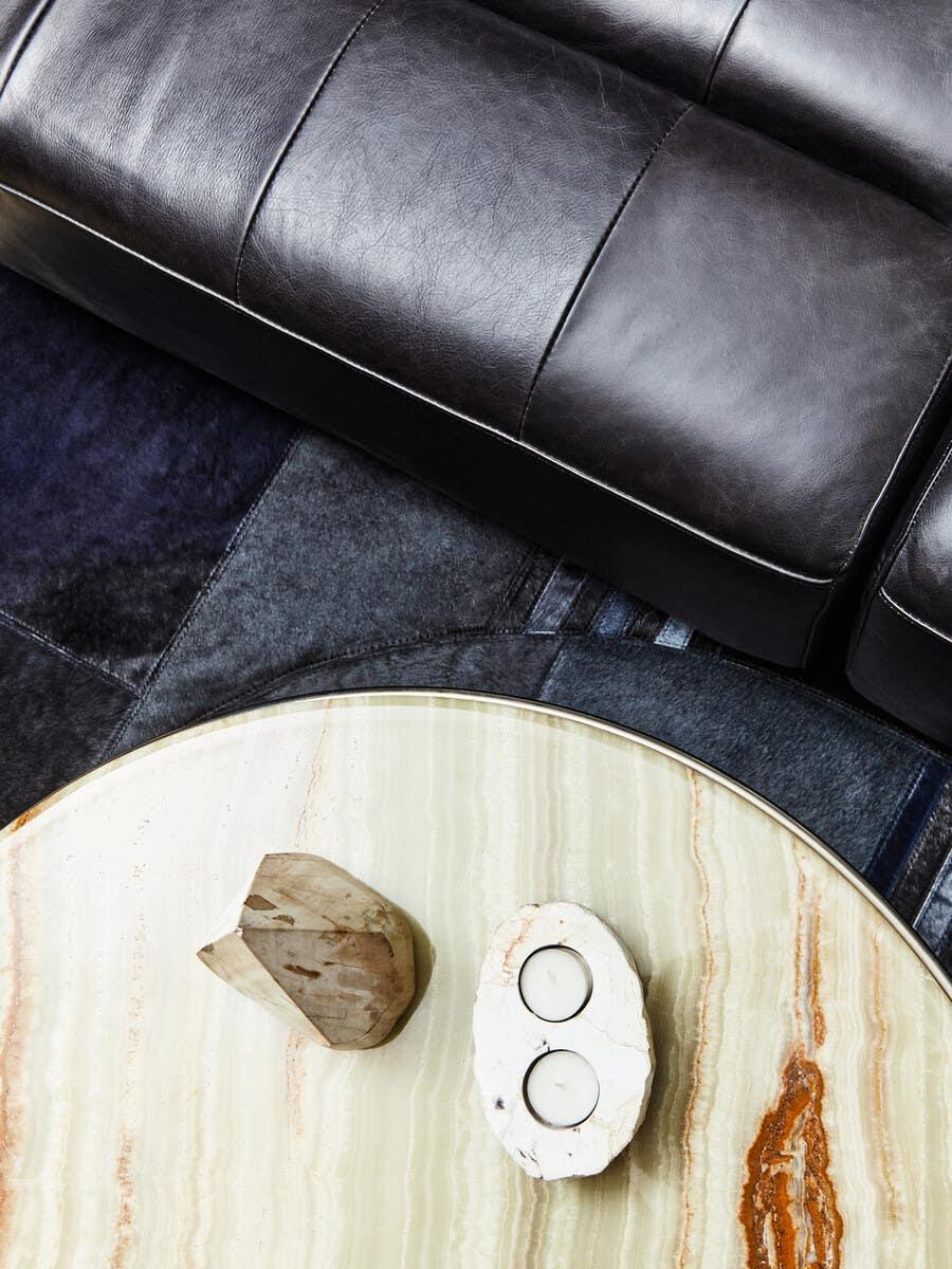 Black leather sofa with marble coffee table and stone candle holder on dark rug