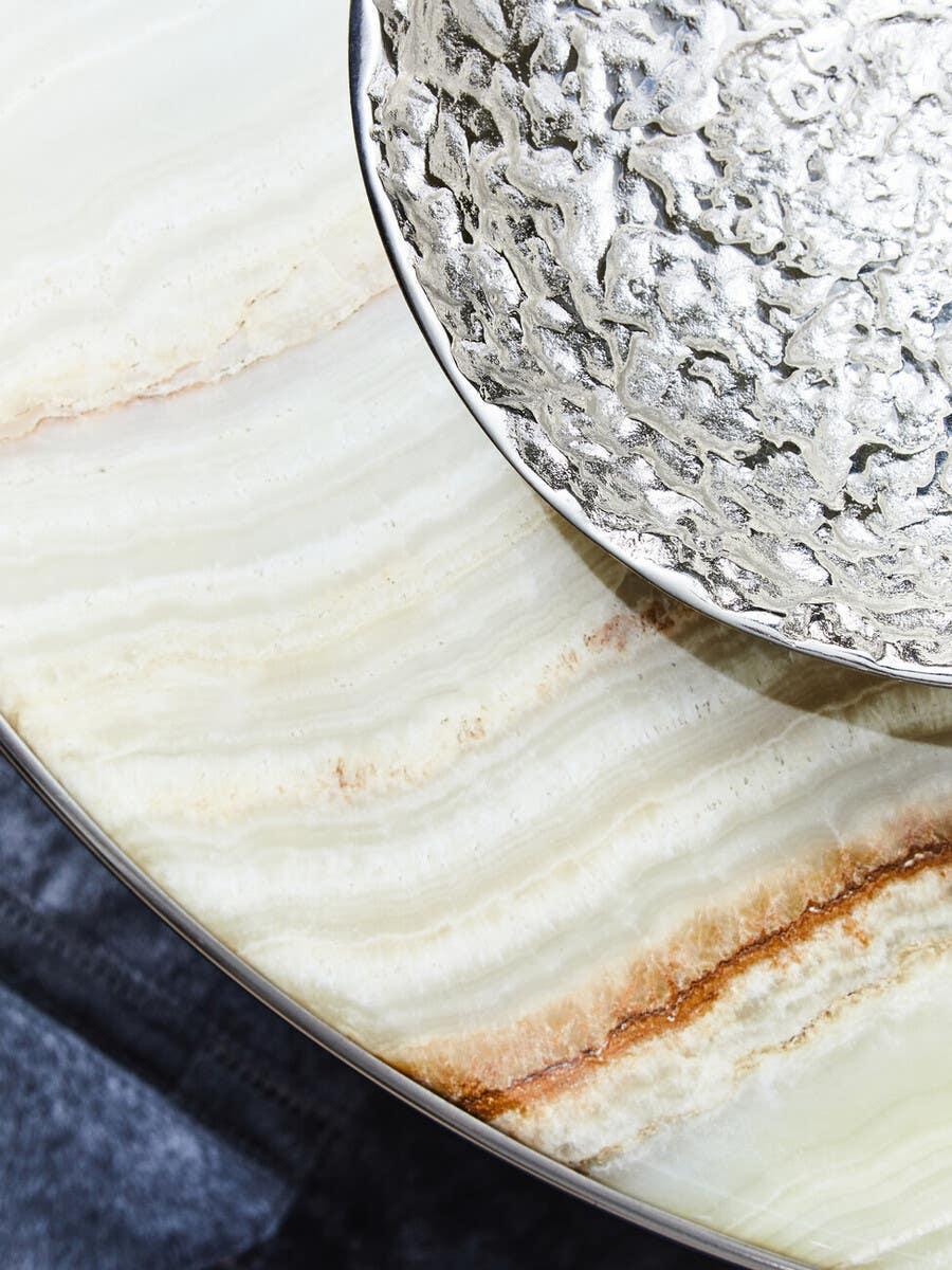 Round marble coffee table with silver hammered metal bowl on top, close-up view