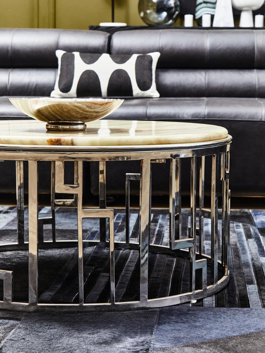 Round marble coffee table with chrome geometric base on modern rug in front of leather sofa