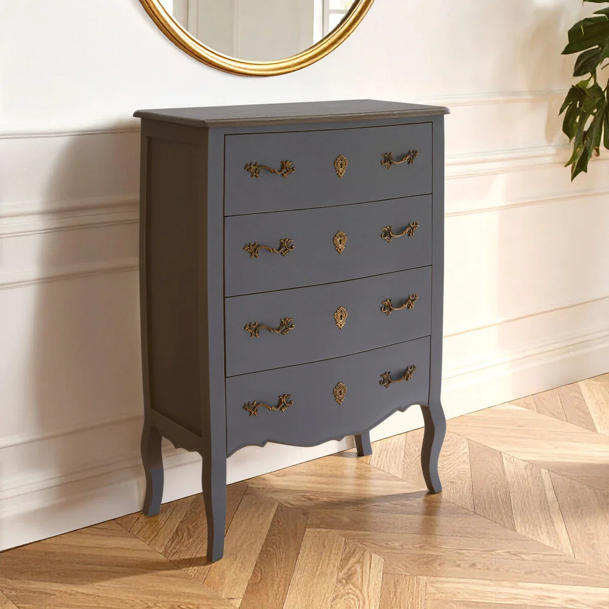 Grey chest of drawers with ornate brass handles in a bright room with wooden flooring