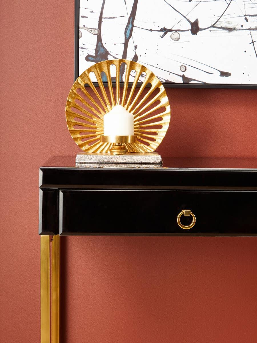 Gold decorative candle holder on black console table against terracotta wall