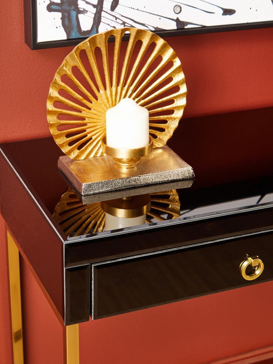 Gold metal candle holder with pillar candle on glossy black console table