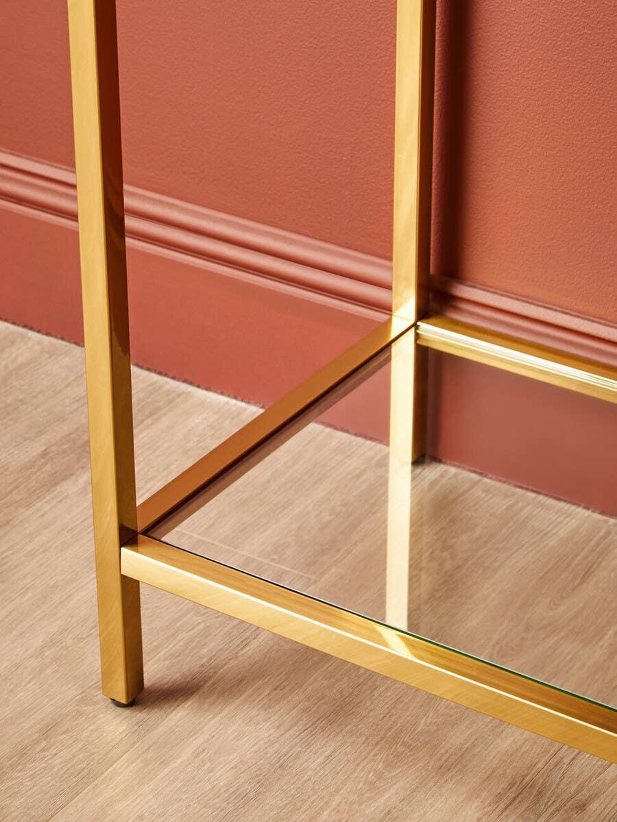 Gold metal console table frame with glass shelf on wood floor against terracotta wall