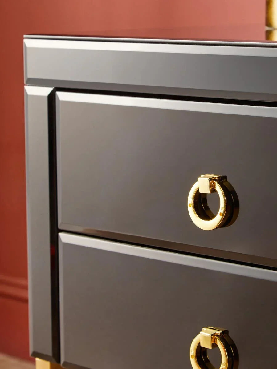 Black gloss bedside table with gold ring drawer handles against a red wall