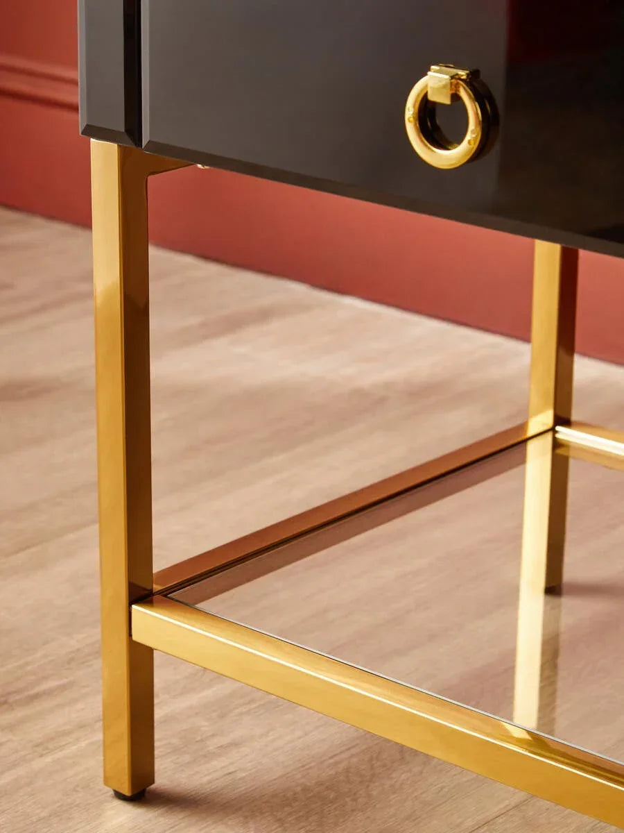 Black and gold bedside table with metal legs and gold ring handle on wood floor