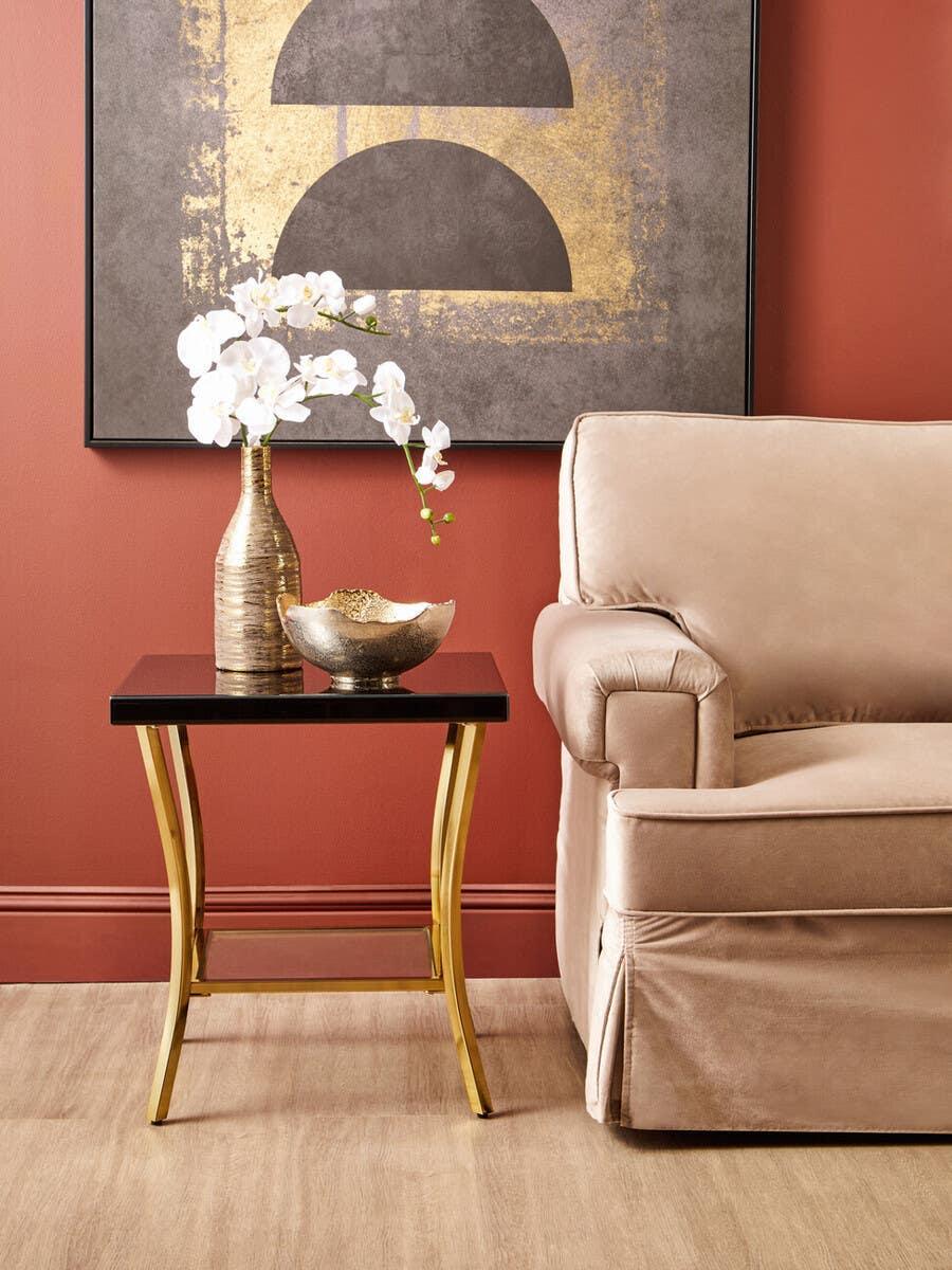 Gold and black side table with metallic vase and ornaments beside beige sofa in living room