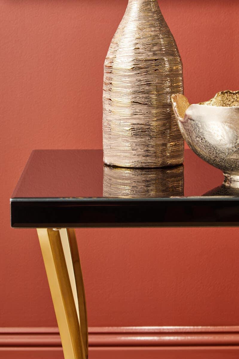 Black glass side table with gold metal legs and metallic vase against terracotta wall