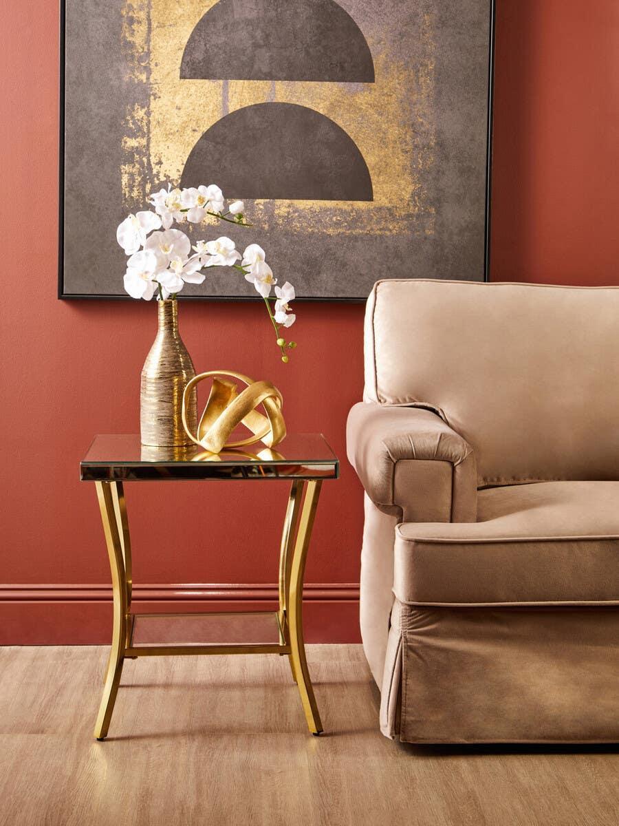 Gold metal and glass side table with decorative vase beside beige sofa in modern living room