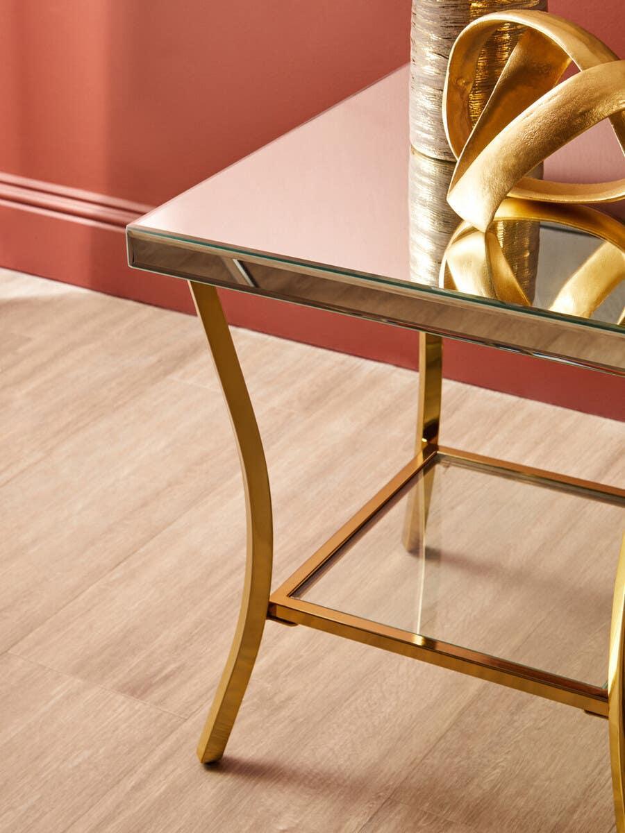 Gold metal and glass side table with decorative items, set against a wooden floor