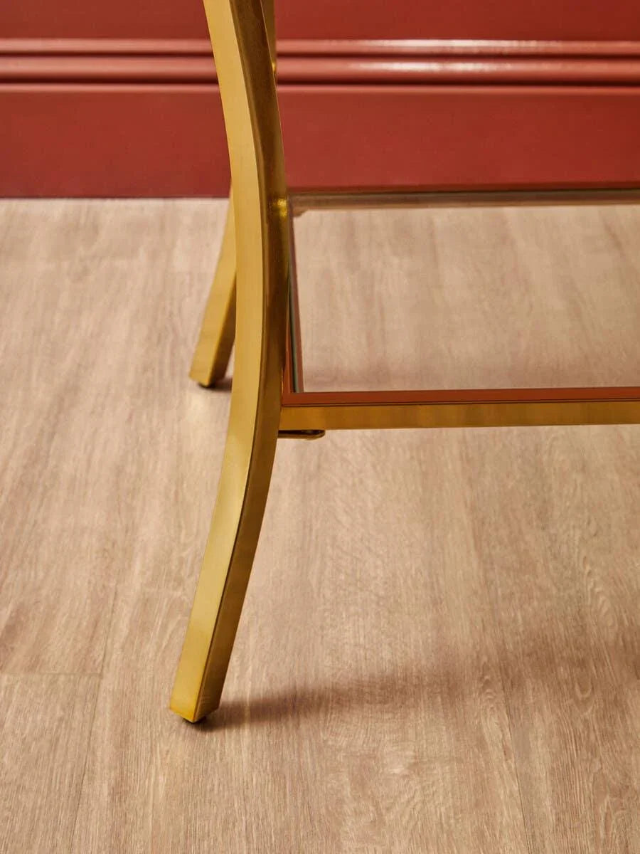 Gold metal table leg with glass shelf on wood flooring near red wall