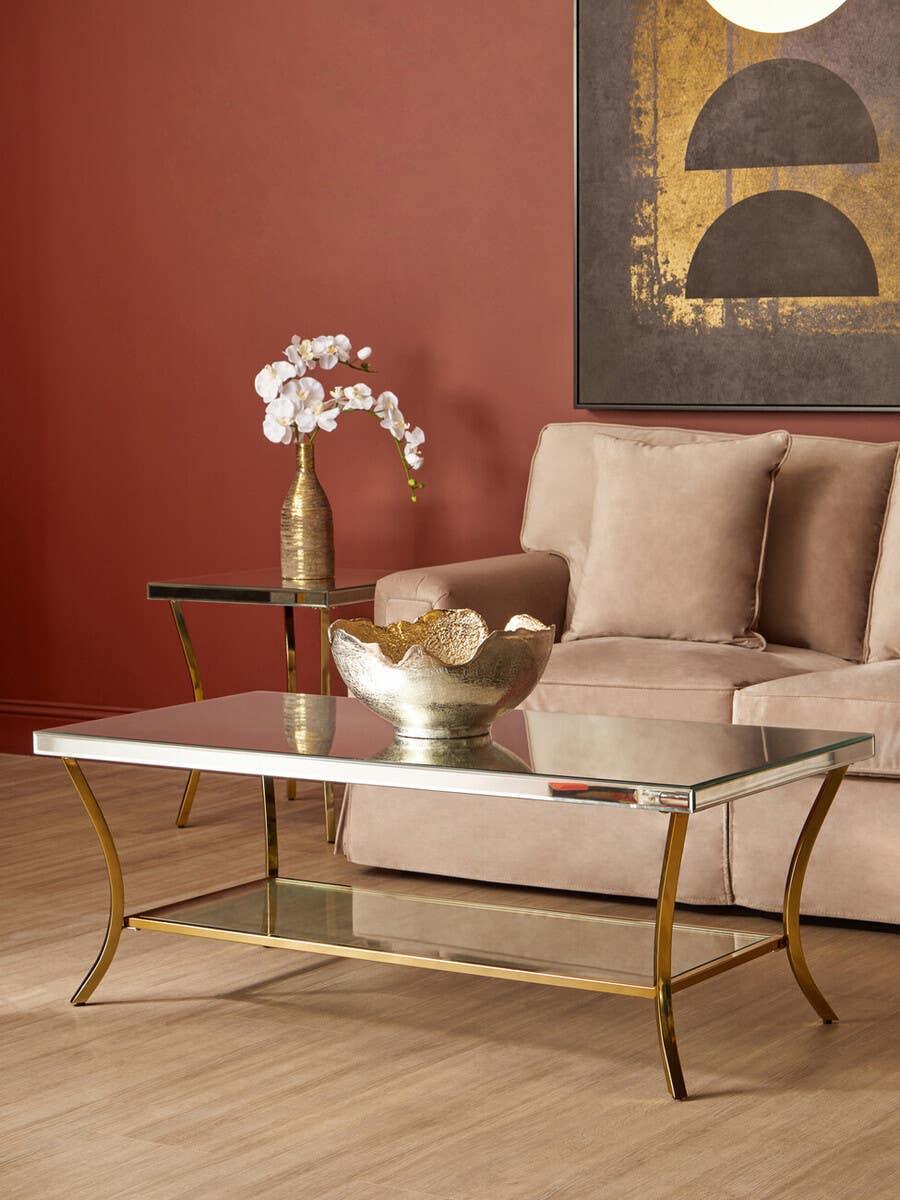 Glass coffee table with gold metal legs in living room with beige sofa and modern decor