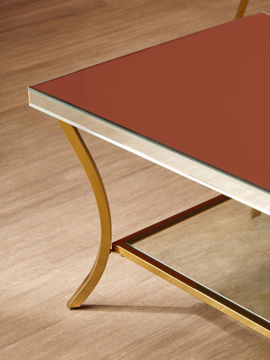 Glass coffee table with gold metal frame and angled leg on wooden floor