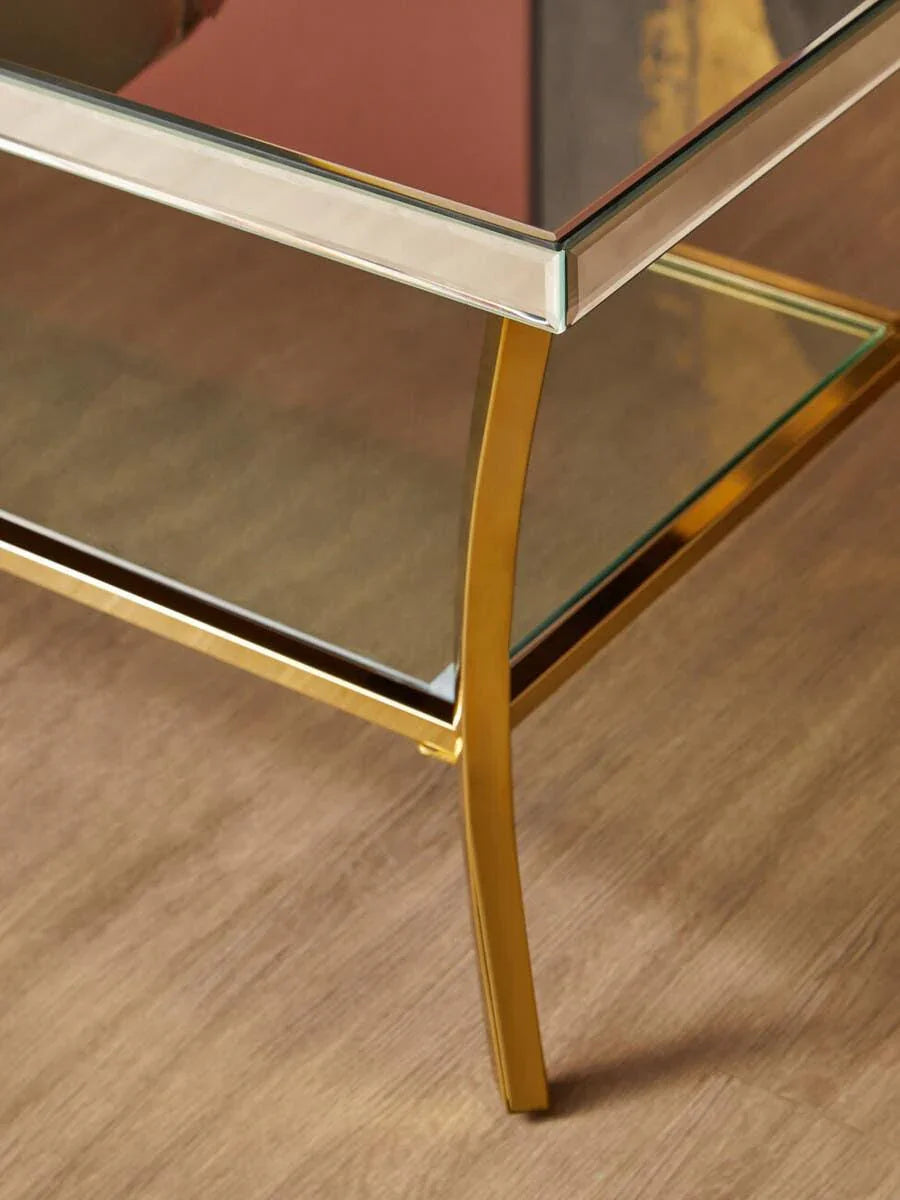 Glass coffee table with gold metal frame and shelf on wooden floor