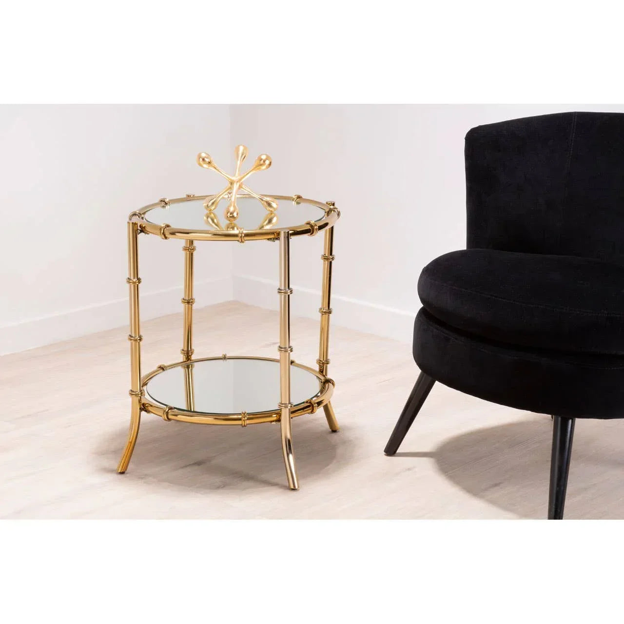 Round gold metal side table with mirrored shelves beside black velvet chair