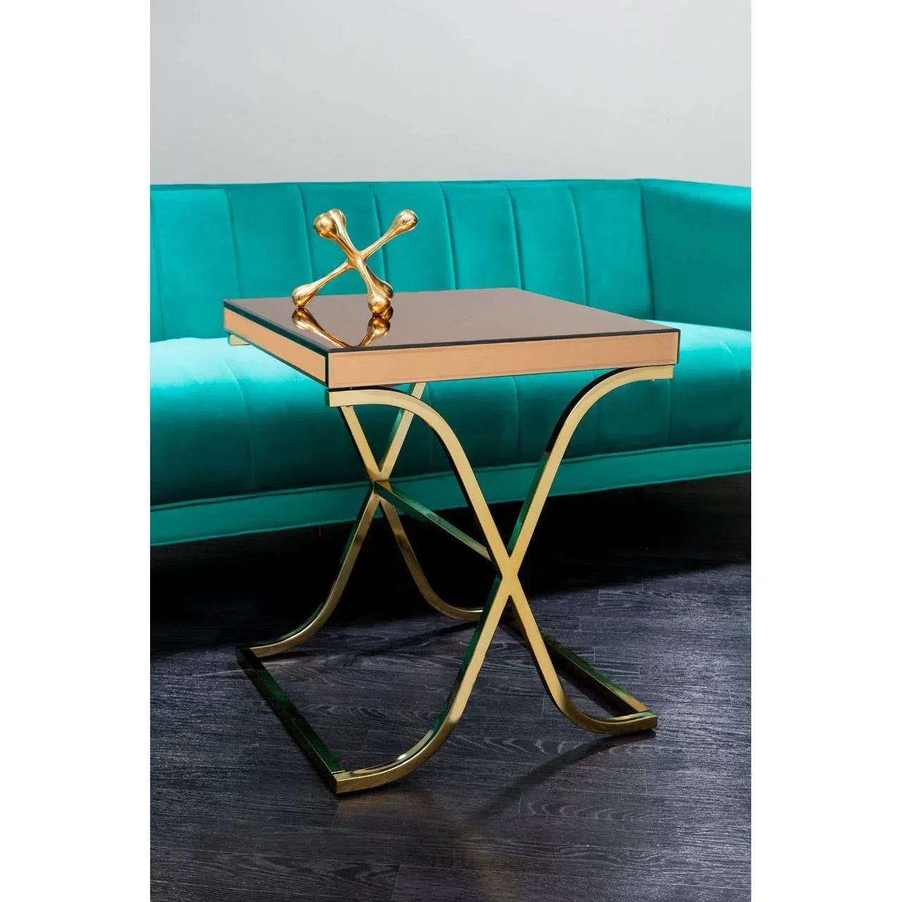 Gold metal side table with mirrored top beside teal sofa on dark wood floor