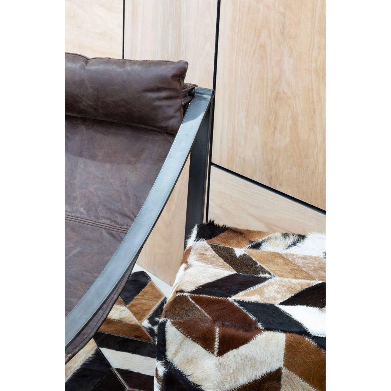 Brown leather armchair with metal frame beside geometric cowhide footstool